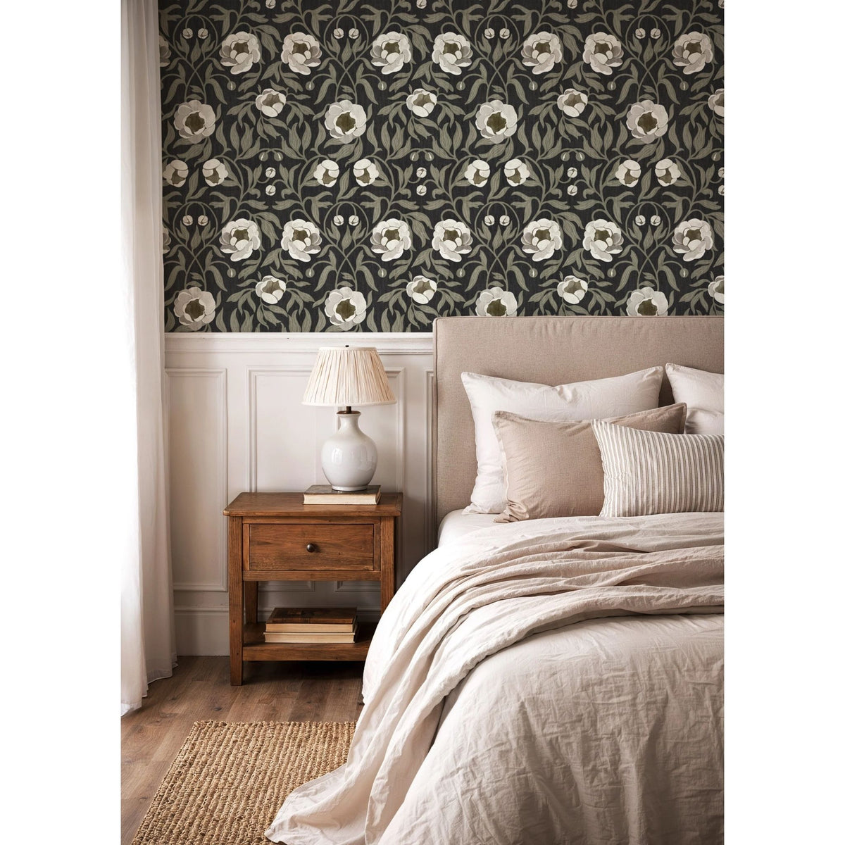 Summer Gray Peony Charcoal bloemenbehang boven witte lambrisering achter een beige bed met houten nachtkastje